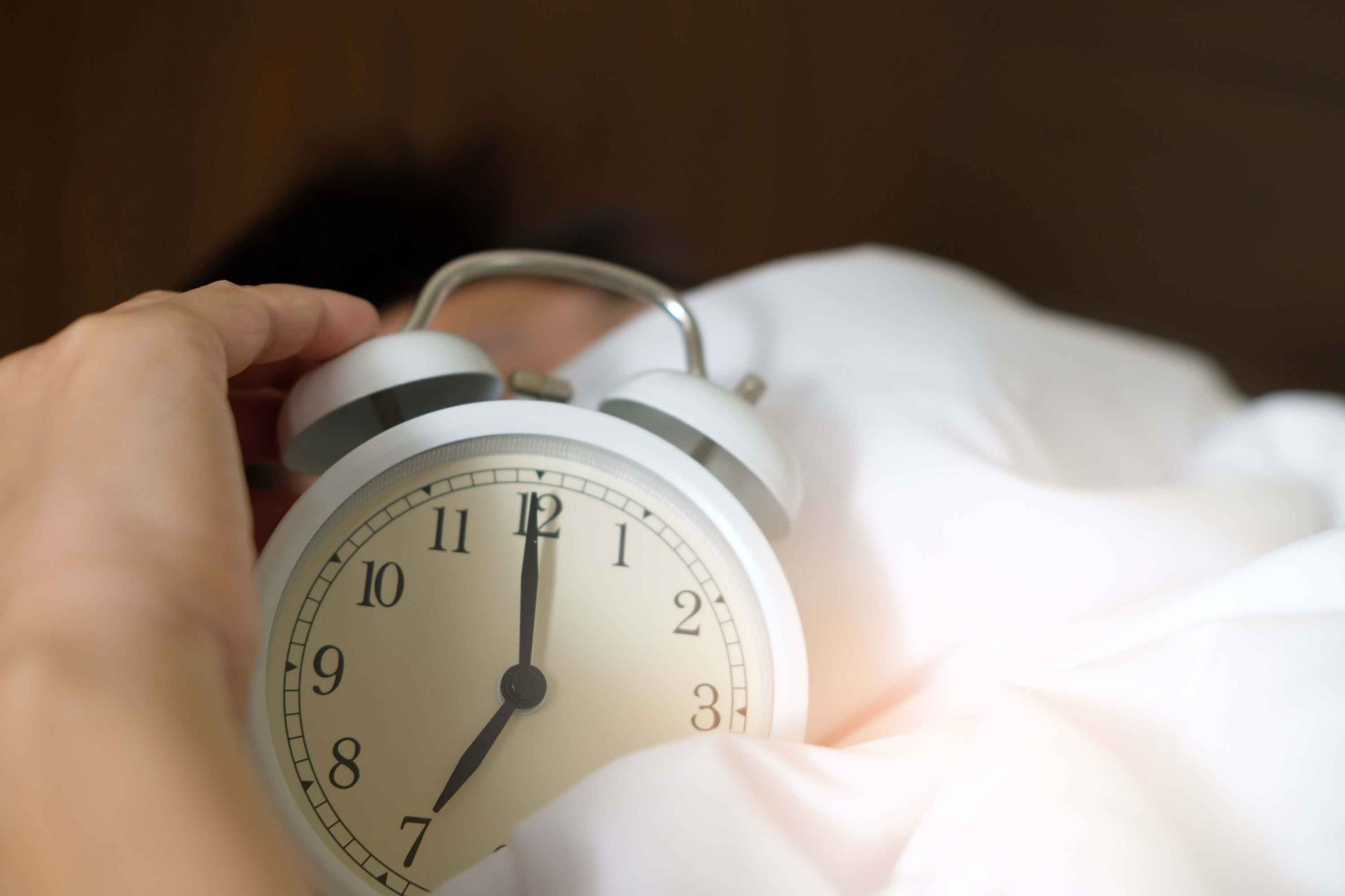 Alarm clock in hands in bed sheets