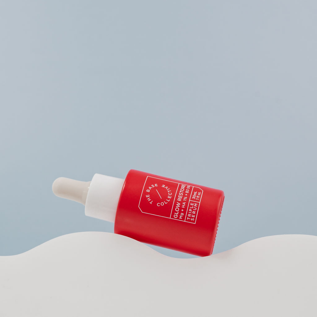 Glow Niacinamide serum with Hyaluronic Acid & Magnesium by The Base Collective on side lying on cloud