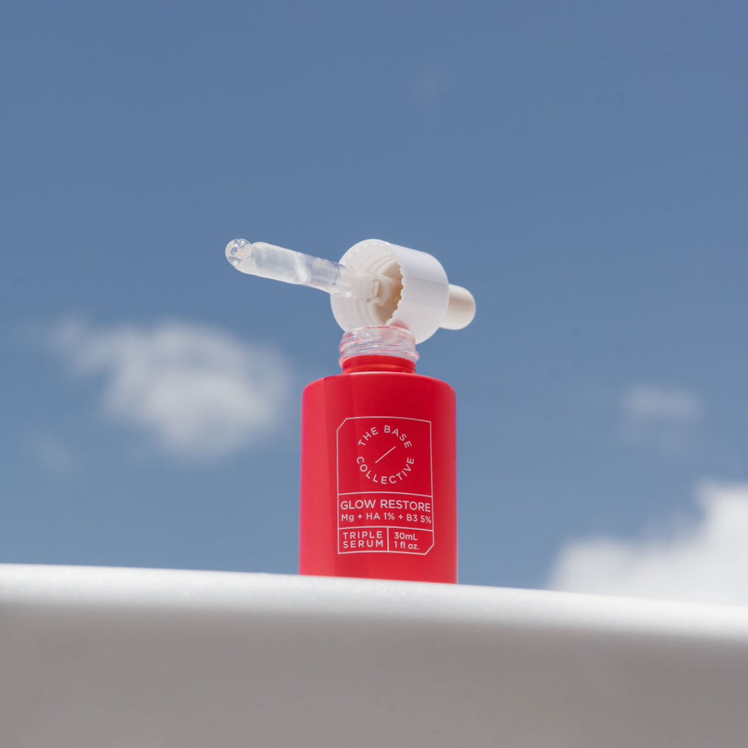 Glow Niacinamide Serum with Hyaluronic Acid and Magnesium by The Base Collective open bottle on ledge with sky background