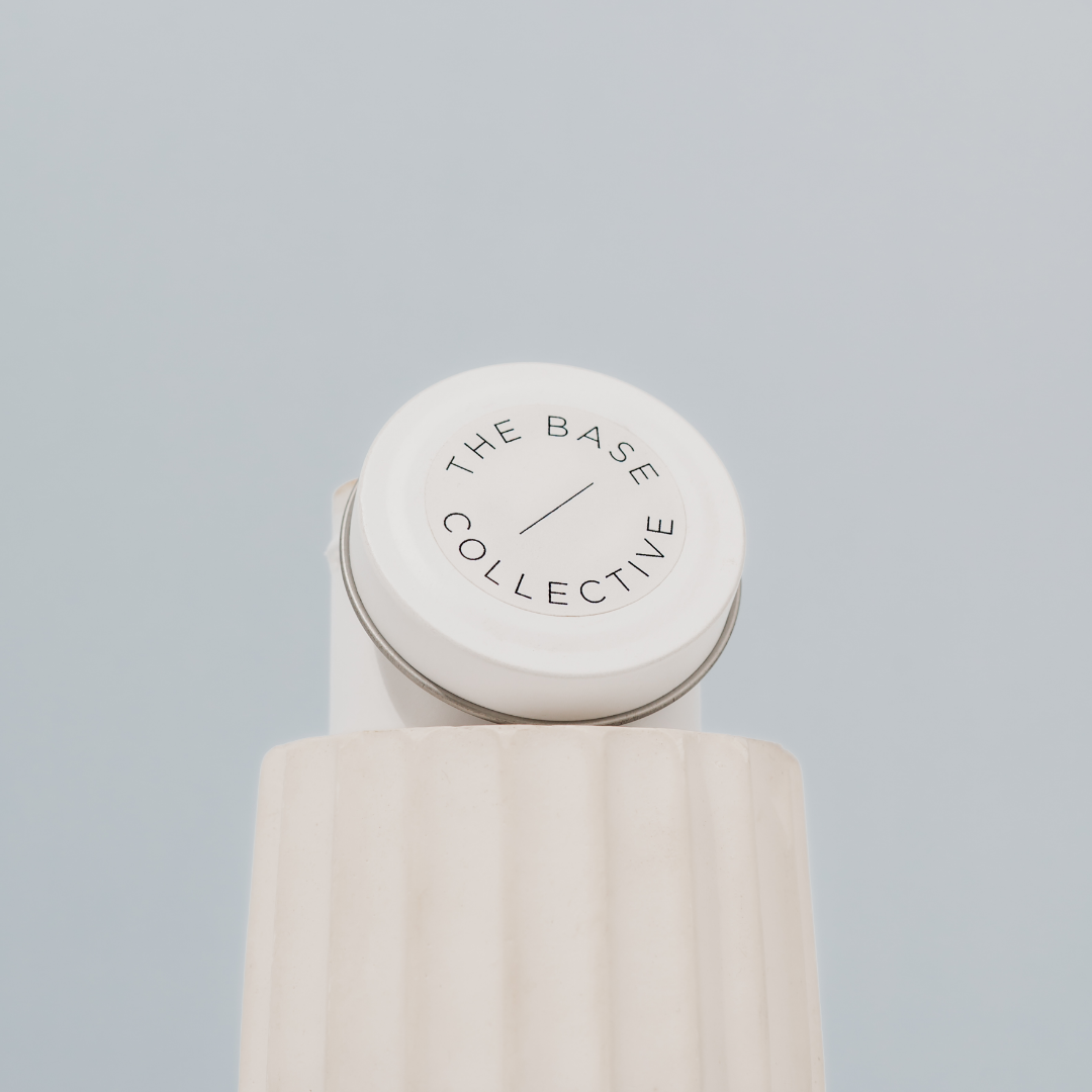 Scented Soy Candle by The Base Collective travel tin on white pillar, top of lid against blue background.