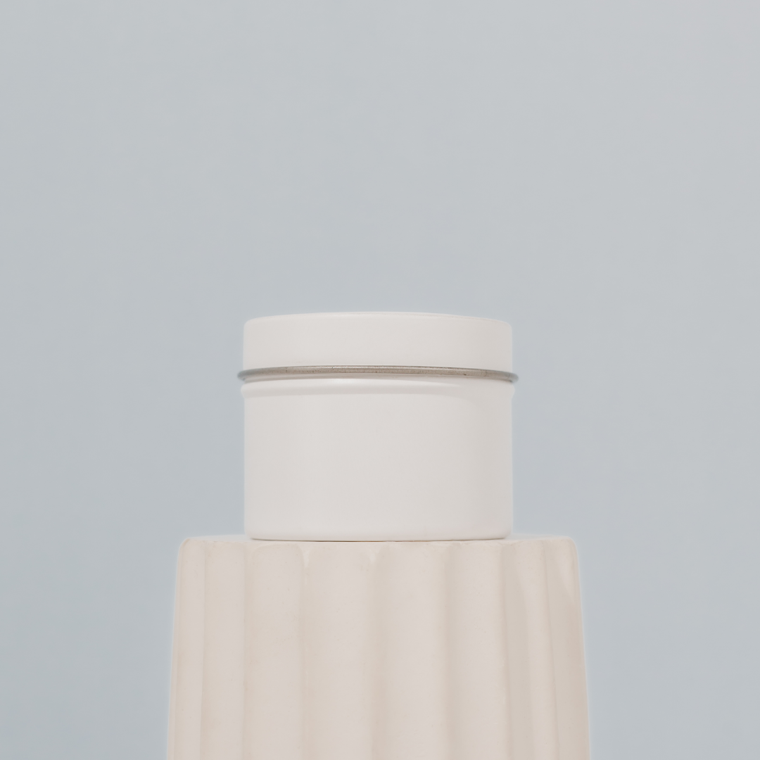 Scented soy candle by The Base Collective, side of tin on white pillar against blue background.