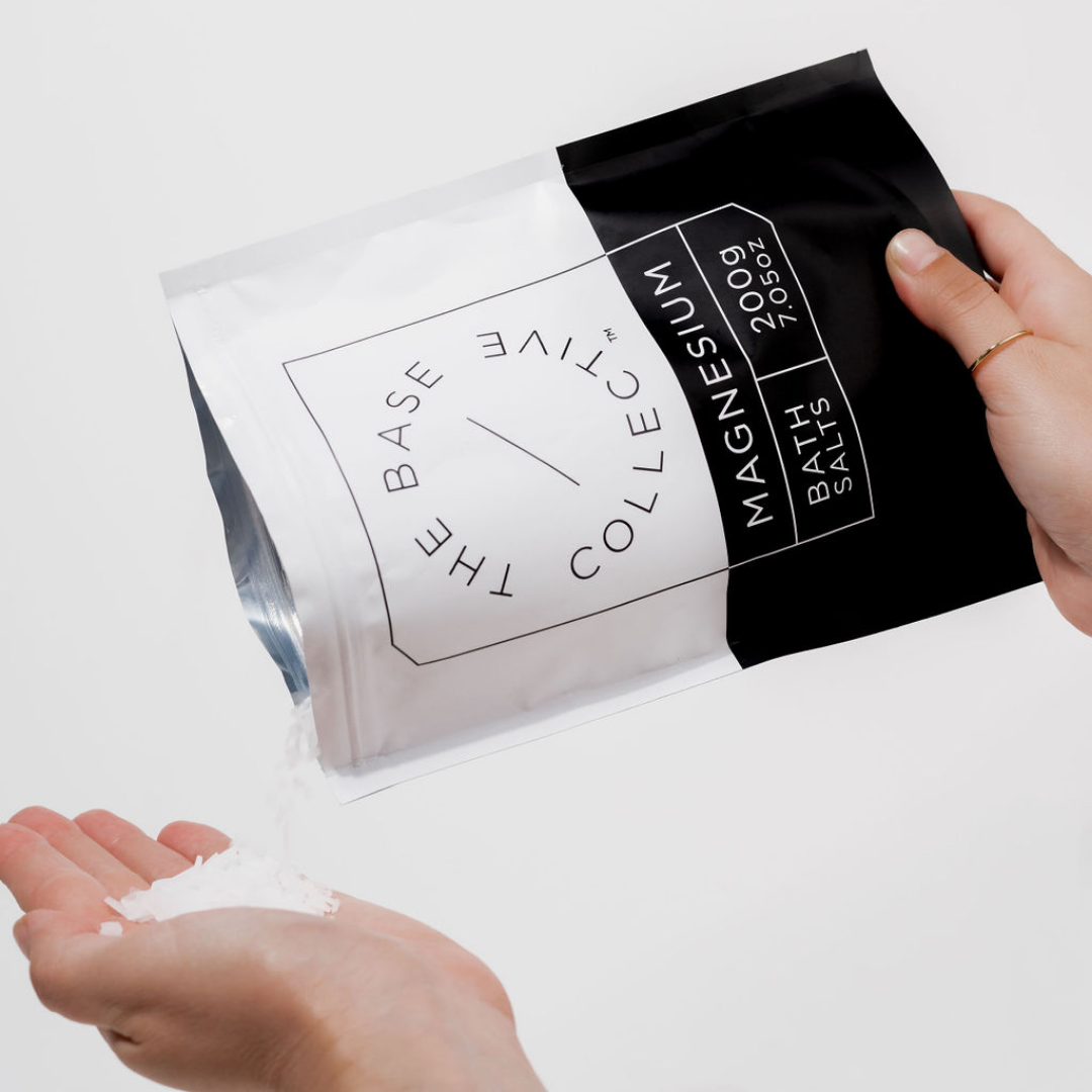 Magnesium Chloride Flakes by The Base Collective open packet pouring into an open palm against white background.