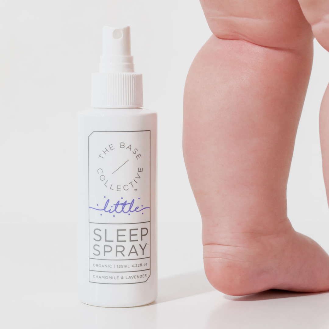 Little Lavender Sleep Spray with chubby baby leg next to it against a white background. 