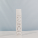 Sunscreen by The Base Collective with water drops on it against a blue background.