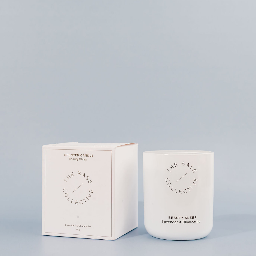Beauty Sleep Scented Soy Candle by The Base Collective, candle beside closed box against light blue background.