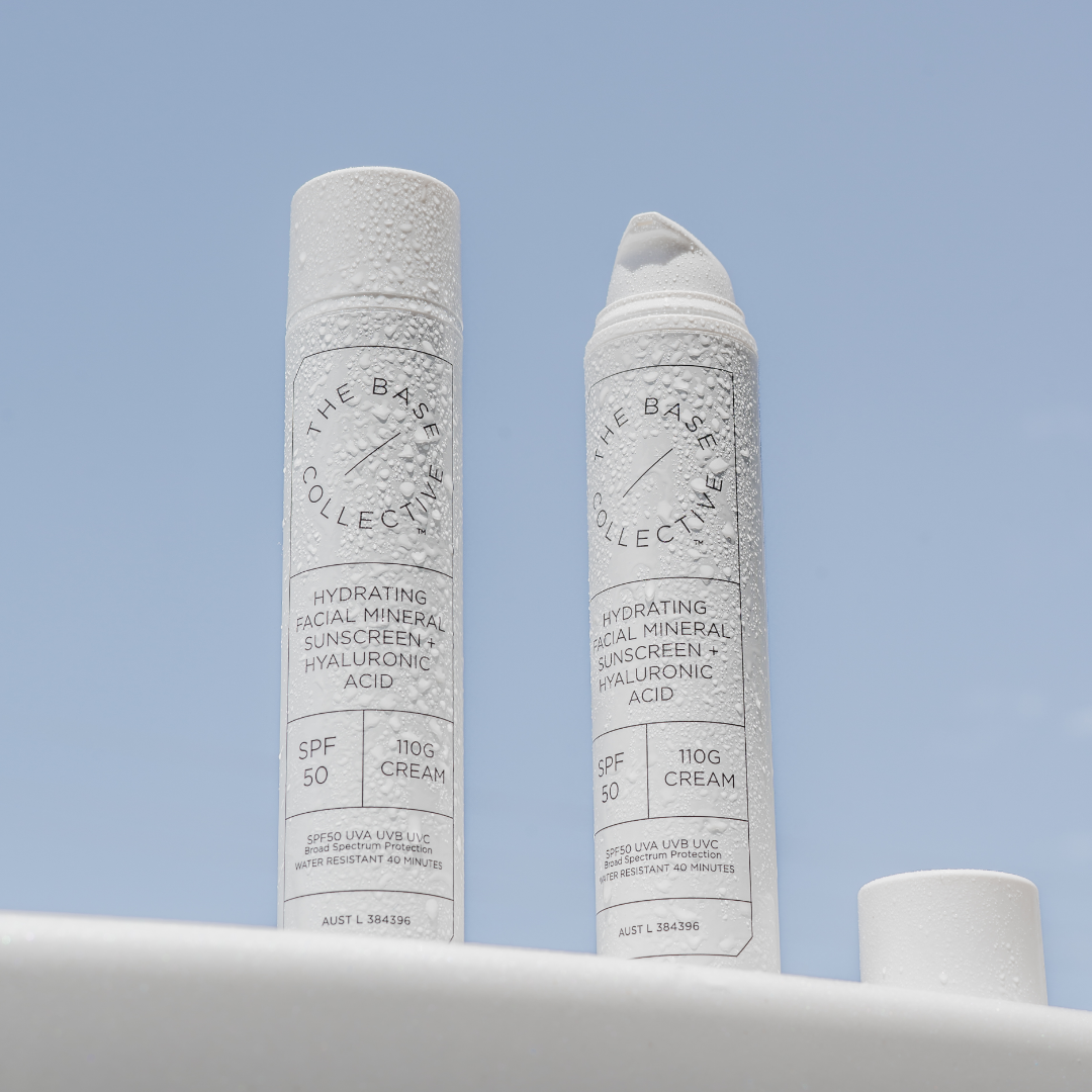 SPF50 Mineral tinted face sunscreen two bottles, with water drops on them against a blue background.