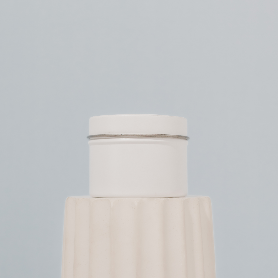 Scented soy candle by The Base Collective, side of tin on white pillar against blue background. 